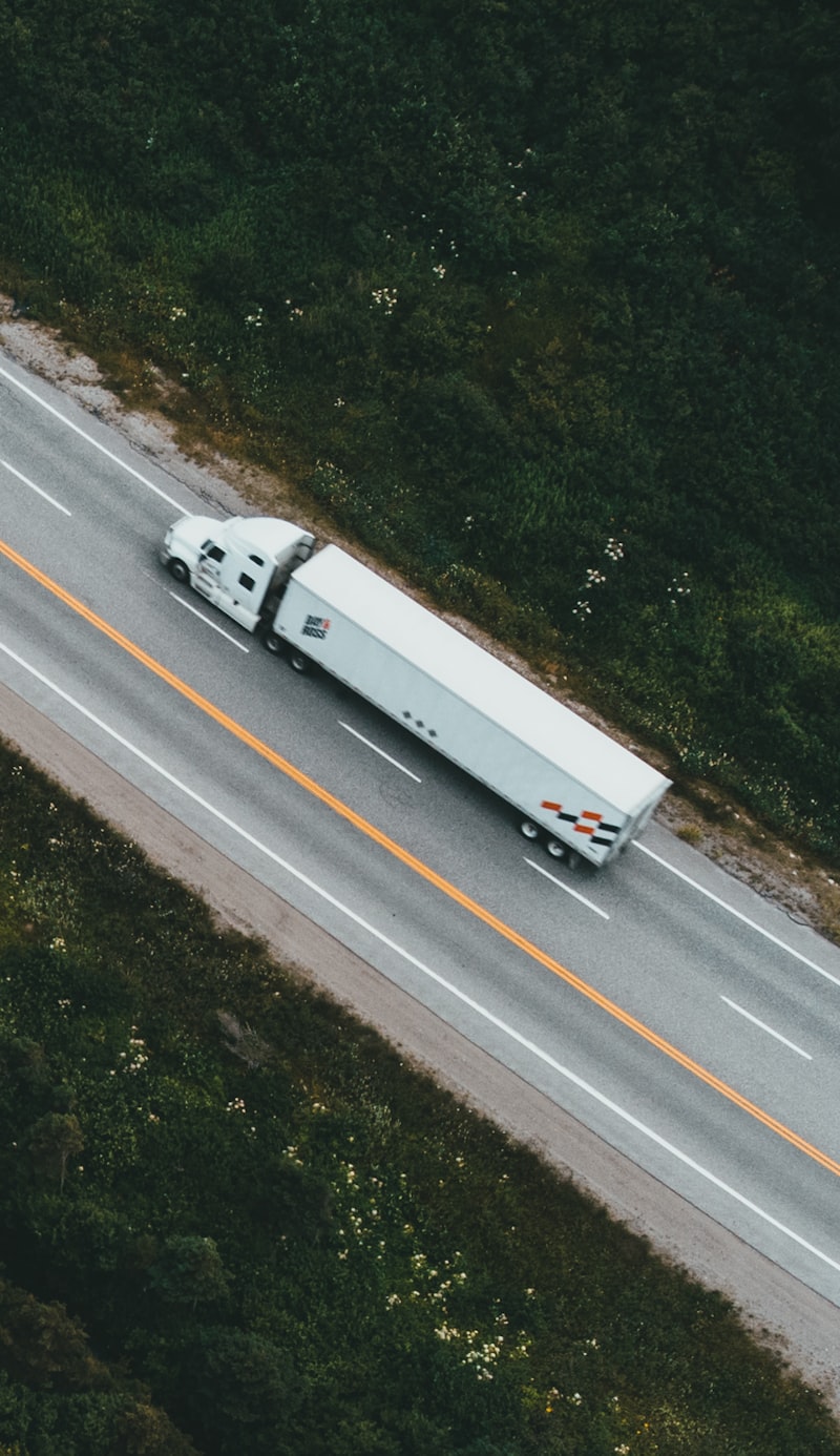 Aerial view of a semi-truck traveling along a road bordered by dense trees